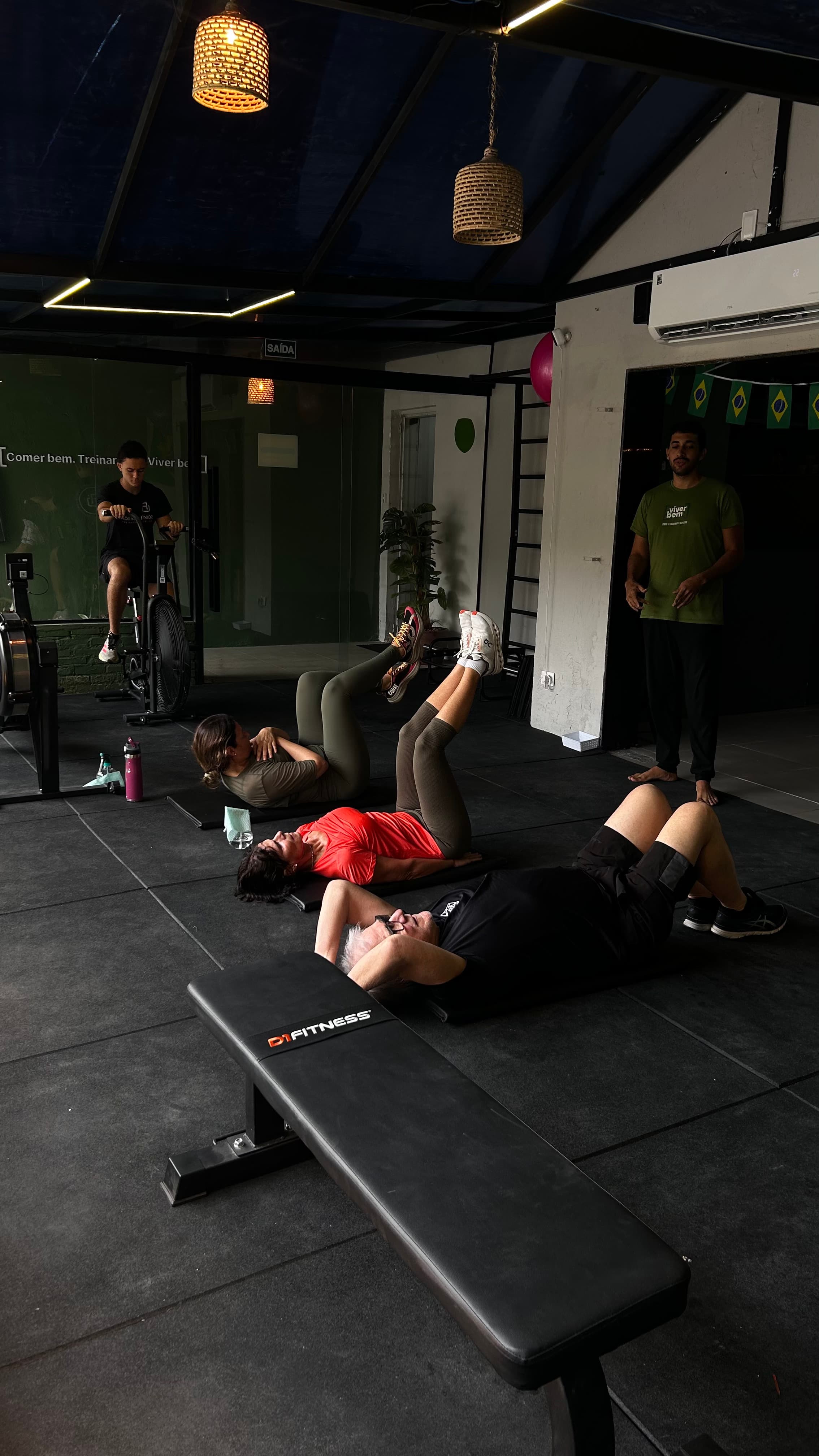 Pessoas fazendo exercícios abdominais em colchonetes em uma academia enquanto um instrutor as observa.