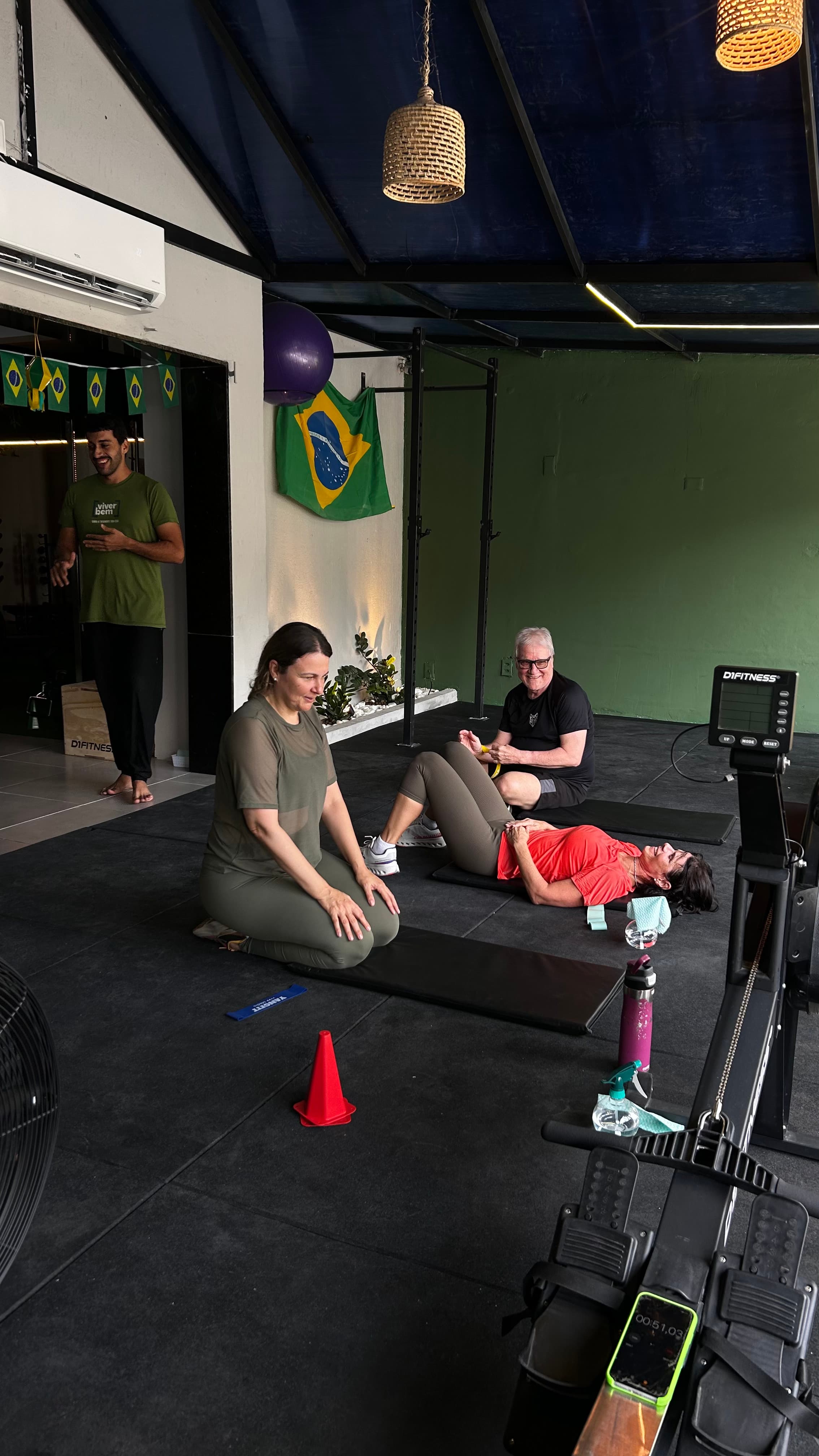 Pessoas se exercitando em colchonetes em uma academia decorada com a bandeira do Brasil.