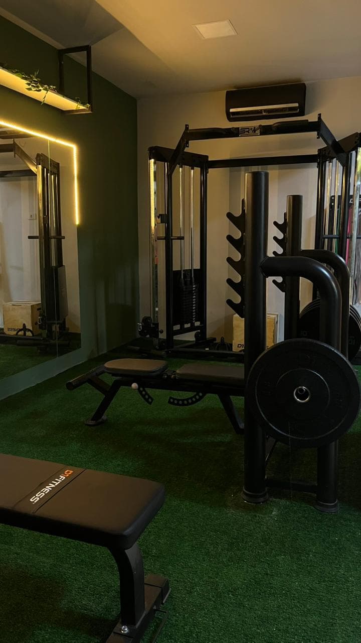 Academia com grama sintética verde, equipamentos de musculação pretos e iluminação quente em ambiente moderno.